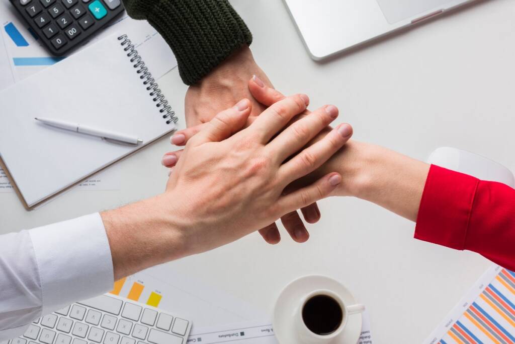 Mani unite tra colleghi in ufficio, simbolo di collaborazione e welfare aziendale.