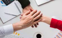 Mani unite tra colleghi in ufficio, simbolo di collaborazione e welfare aziendale.