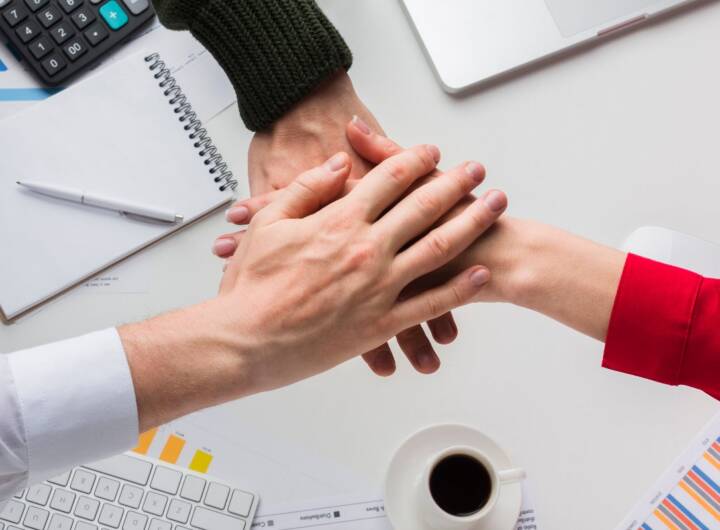 Mani unite tra colleghi in ufficio, simbolo di collaborazione e welfare aziendale.