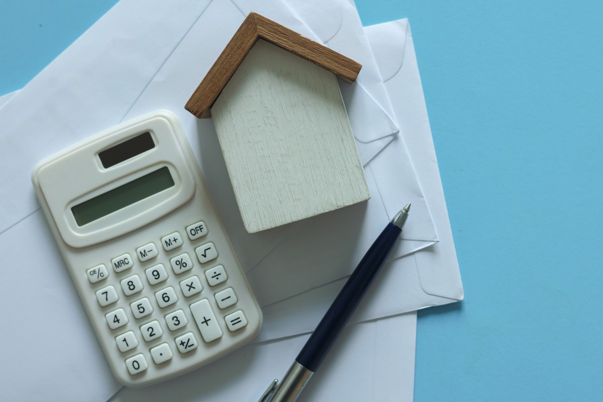 Calcolatrice, modello di casa e fogli su un tavolo.